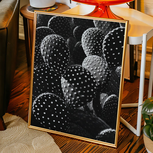 Framed artwork of cacti on a wooden floor with a chair and plants in the background