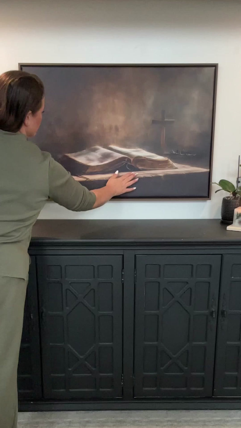 Ashley hanging her framed Kooly Bible and cross canvas above a sideboard