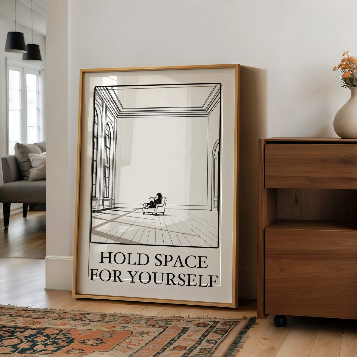 A Room Kept Open for You, a fine black line drawing of a tall empty room with a long floor, a pale window and a small seated figure, with the serif words HOLD SPACE and FOR YOURSELF beneath it on a cream ground, in a wood frame on a wall beside a walnut cabinet and an open doorway
