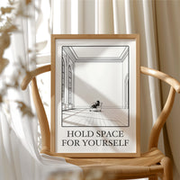 A Room Kept Open for You, a fine black line drawing of a tall empty room with a long floor, a pale window and a small seated figure, with the serif words HOLD SPACE and FOR YOURSELF beneath it on a cream ground, in a wood frame beside a wicker chair by a sunny window