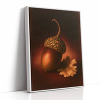 A Single Acorn in Candlelight, one acorn resting beside a curled oak leaf on a dark brown ground, lit from one side and painted in chestnut, amber and deep shadow, as a framed canvas in a white frame