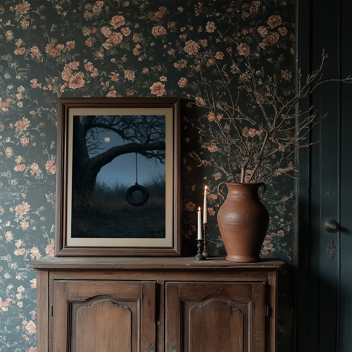 A Swing Left for the Moon, a bare tree with a dark tire swing hanging beneath a pale moon in a blue dusk field, painted in slate, midnight blue and moonlit cream, in a dark frame on a wooden dresser against floral wallpaper