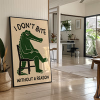 Bites Only With a Reason, a crocodile sitting upright in a plain wooden chair, in deep green on a cream ground, with a bold lettered line above reading I DON'T BITE and one below reading WITHOUT A REASON, in a black frame leaning on a bright hallway floor beside a potted plant