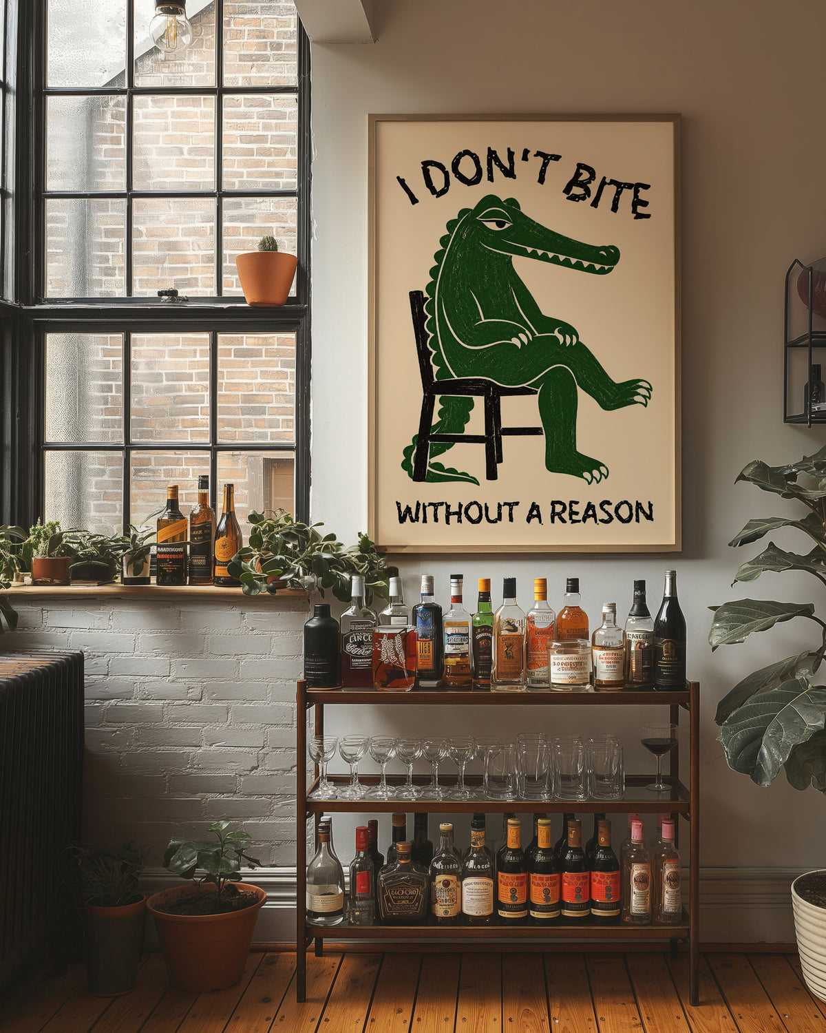 Bites Only With a Reason, a crocodile sitting upright in a plain wooden chair, in deep green on a cream ground, with a bold lettered line above reading I DON'T BITE and one below reading WITHOUT A REASON, in a wood frame on a brick wall above a bar cart of bottles and plants
