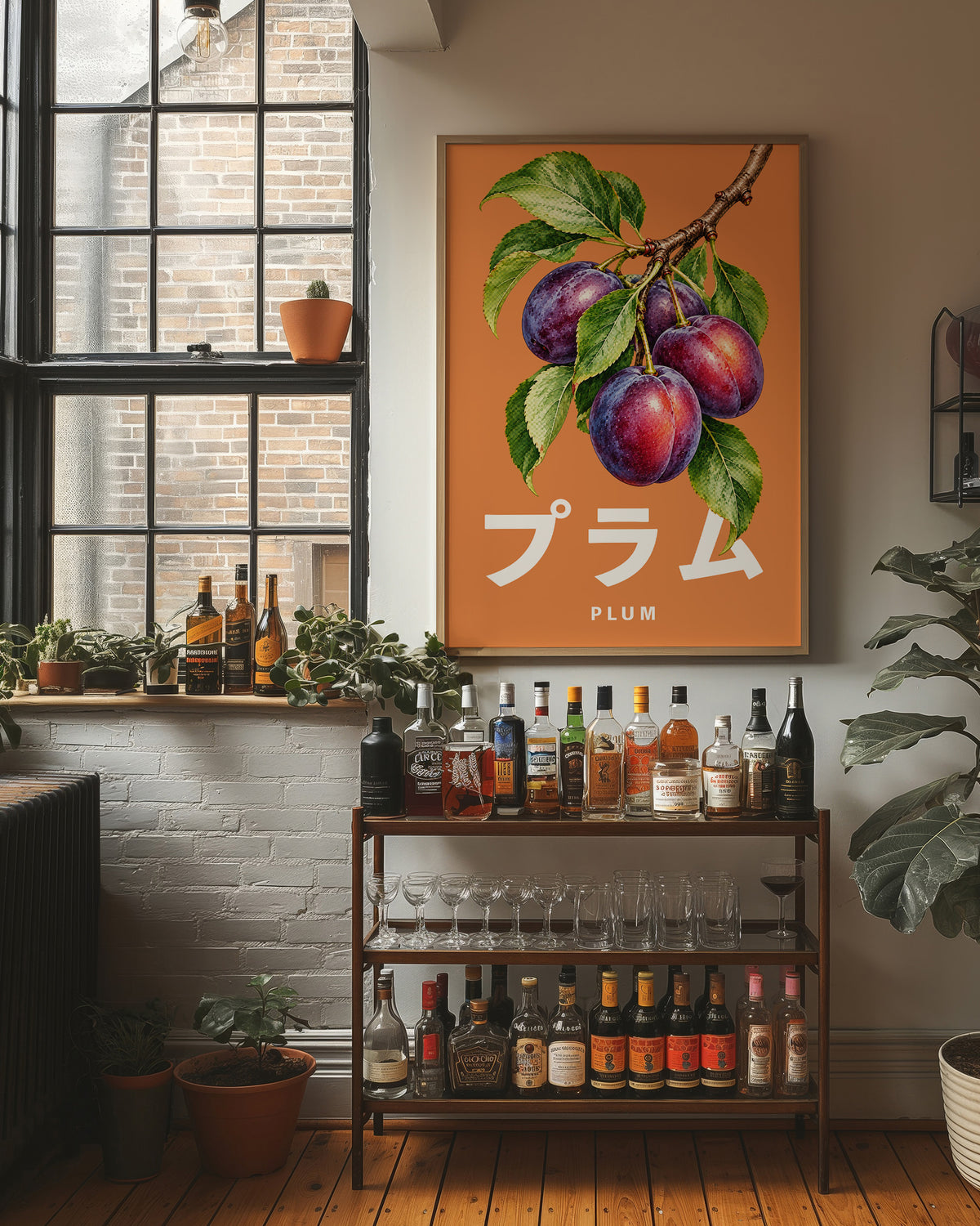 Branch Heavy with Plums, a branch of purple plums with green leaves on a burnt orange ground, with a tall block of Japanese katakana and the English word PLUM set small in cream beneath, in a wood frame on a brick wall above a bar cart of bottles and plants