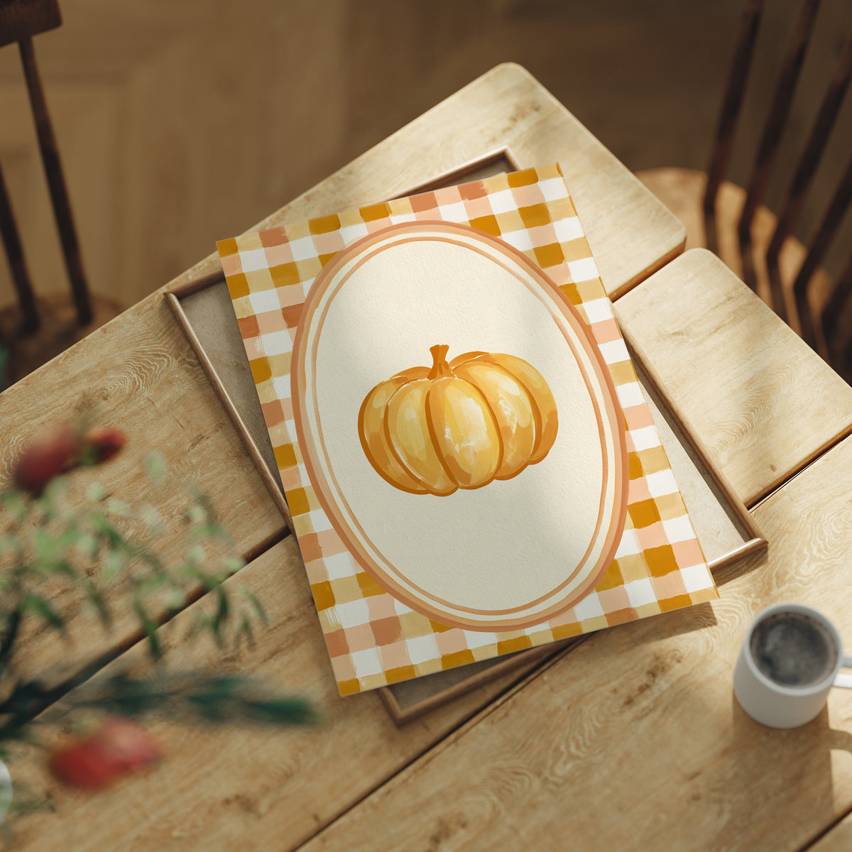 Dressed Up for a Quiet Afternoon, a single orange pumpkin in a cream oval medallion framed by a yellow and rust gingham border, painted in mustard, cream and burnt orange, lying flat on a light wood table beside a coffee cup and red berries