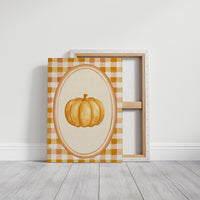 Dressed Up for a Quiet Afternoon, a single orange pumpkin in a cream oval medallion framed by a yellow and rust gingham border, painted in mustard, cream and burnt orange, on a gallery canvas with wrapped edges leaning against a white wall