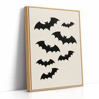 Evening Flight in Silhouette, a loose flock of black bat silhouettes spread across a cream ground in a simple, flat graphic arrangement, as a framed canvas in a natural wood frame