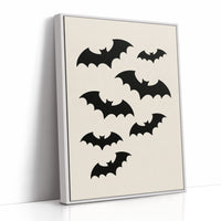 Evening Flight in Silhouette, a loose flock of black bat silhouettes spread across a cream ground in a simple, flat graphic arrangement, as a framed canvas in a white frame