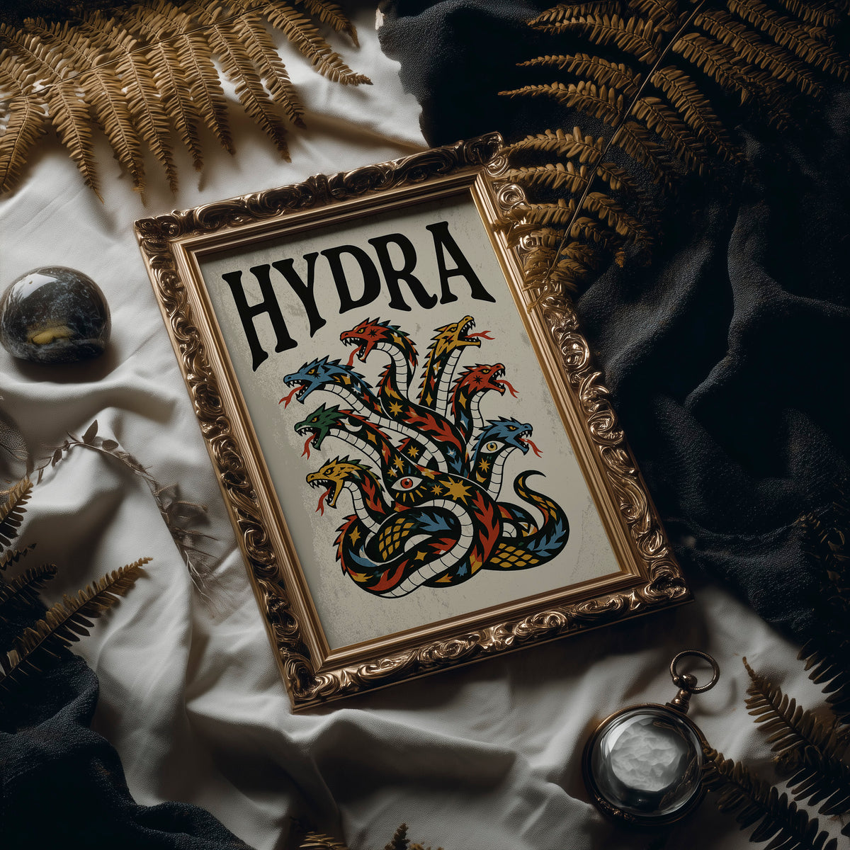 Every Head Grows Back Bolder, a many headed serpent with blue, red and gold scales rising in fans of heads, in a bold flash sheet style with a black lettered name across the top on a cream ground, in an ornate frame on silk cloth beside ferns and a brass compass