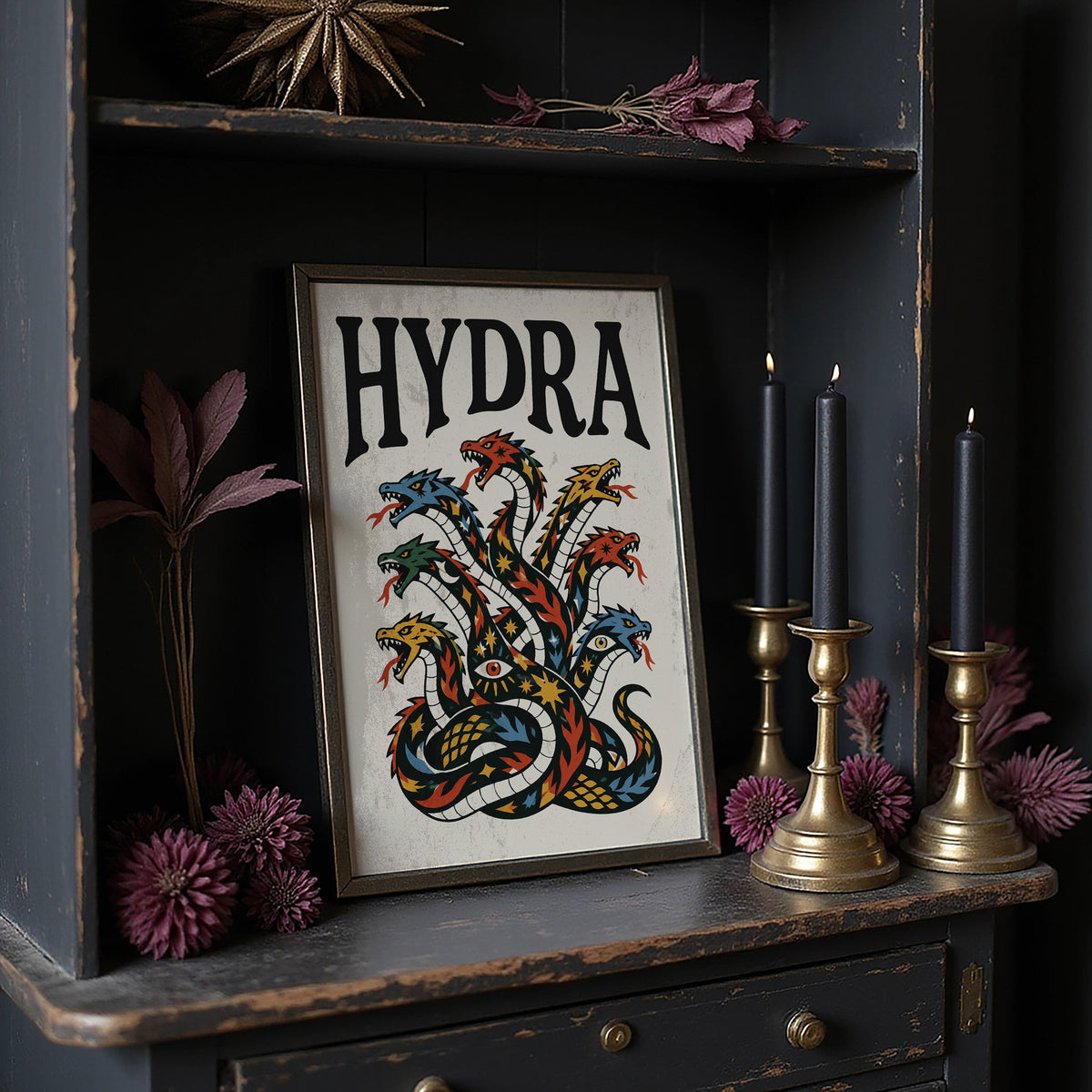 Every Head Grows Back Bolder, a many headed serpent with blue, red and gold scales rising in fans of heads, in a bold flash sheet style with a black lettered name across the top on a cream ground, in a dark frame on a black shelf beside brass candles and dried leaves
