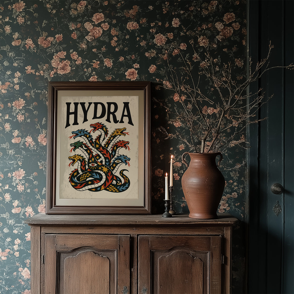 Every Head Grows Back Bolder, a many headed serpent with blue, red and gold scales rising in fans of heads, in a bold flash sheet style with a black lettered name across the top on a cream ground, in a dark wood frame on a floral wallpaper wall above a rustic cabinet and a vase