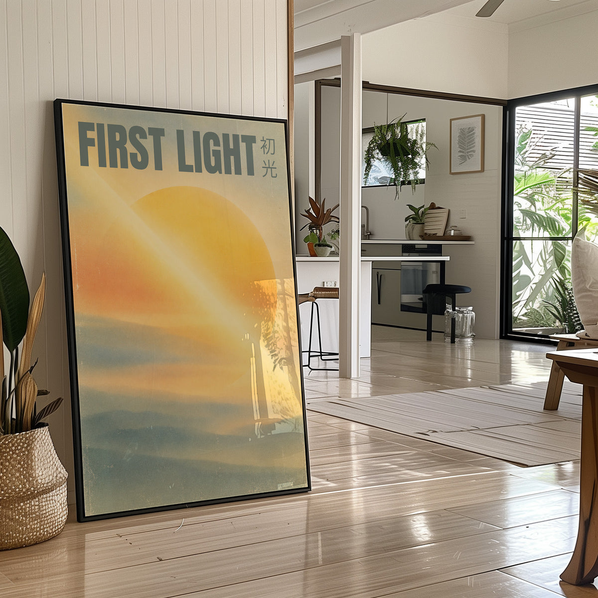 First Light Over a Quiet Sea, a pale sunrise over a soft sea, a warm yellow sun glowing above a band of blue water and peach clouds, with the words FIRST LIGHT in gray capitals across the top and a small Japanese word beside them, in a black frame leaning on a bright hallway floor beside a potted plant