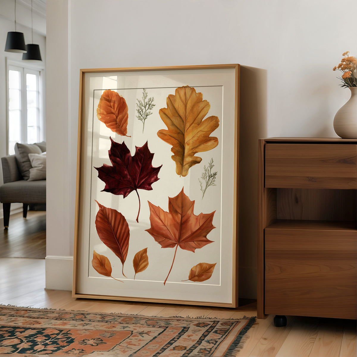 Gold Keeps Its Shape, a cluster of pressed autumn leaves in rust, maroon and gold on a cream ground, drawn in a botanical journal style, in a wood frame on a wall beside a walnut cabinet and an open doorway