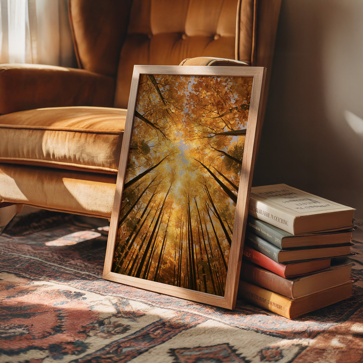 Gold Light Climbs the Tall Trees, a view straight up through tall forest trunks to a canopy lit gold from within, with shafts of warm light falling through the leaves, in amber, deep gold and forest brown, in a wood frame on a rug beside a leather armchair and a stack of books