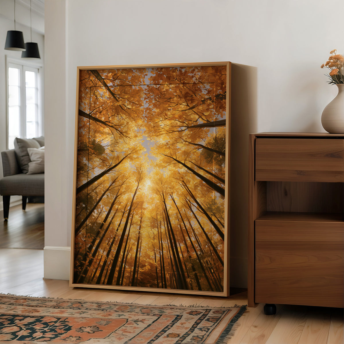 Gold Light Climbs the Tall Trees, a view straight up through tall forest trunks to a canopy lit gold from within, with shafts of warm light falling through the leaves, in amber, deep gold and forest brown, in a wood frame on a wall beside a walnut cabinet and an open doorway