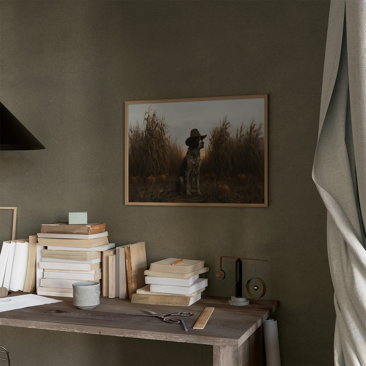 He Guards the Corn Until Dusk, a spotted dog wearing a cowboy hat, sitting in a cornfield among pumpkins under a pale gray evening sky, in a thin wood frame on a moss green wall above a desk stacked with books