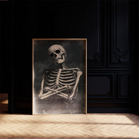 He Keeps His Arms Folded, a seated skeleton with crossed arms and bare ribs against a smoky charcoal ground, painted in bone, charcoal and ash gray, in a dark frame on a black paneled wall above a sunlit herringbone floor