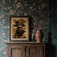 Her Lantern Face Keeps Watch, a witch in a tall pointed hat with a jack o lantern face, draped in a dark cloak with bats and curling vines, on a warm amber parchment ground, painted in ochre, charcoal and burnt orange, in a dark wood frame on a floral wallpaper wall above a rustic cabinet and a vase