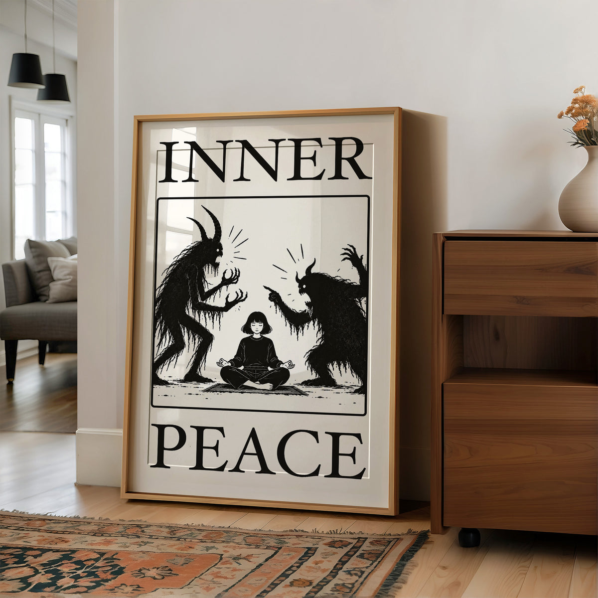Inner Peace Has Company, two horned shadow figures in black flanking a small seated figure meditating at the base, cream ground in a black serif frame, with INNER above and PEACE below, in a wood frame on a wall beside a walnut cabinet and an open doorway
