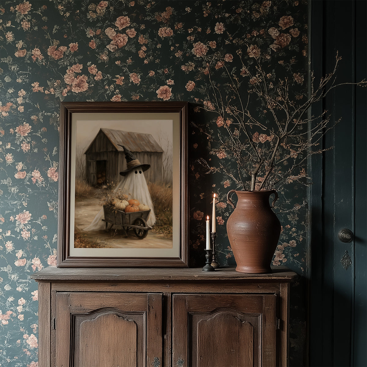 Just Passing Through, Boo, a ghost in a witch hat pushing a wheelbarrow of pumpkins past a weathered shed, painted in straw, gray and pale white, in a dark frame on a wooden dresser against floral wallpaper