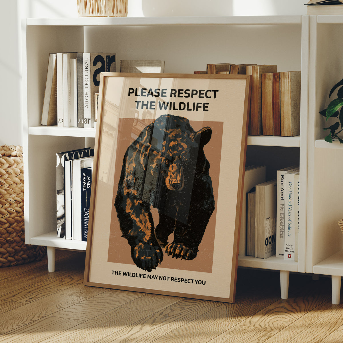 Keep a Respectful Distance, a large black bear with amber and brown fur, head low and shoulders bunched, set on a tan ground under bold black lettering that reads PLEASE RESPECT THE WILDLIFE in a vintage warning sign style, in a wood frame on a white bookshelf beside stacked books and a small basket