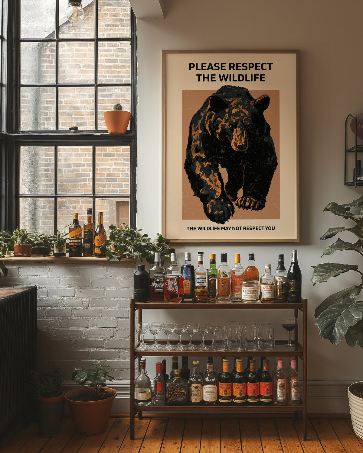 Keep a Respectful Distance, a large black bear with amber and brown fur, head low and shoulders bunched, set on a tan ground under bold black lettering that reads PLEASE RESPECT THE WILDLIFE in a vintage warning sign style, in a wood frame on a brick wall above a bar cart of bottles and plants