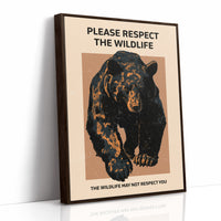 Keep a Respectful Distance, a large black bear with amber and brown fur, head low and shoulders bunched, set on a tan ground under bold black lettering that reads PLEASE RESPECT THE WILDLIFE in a vintage warning sign style, as a framed canvas in a brown frame