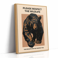 Keep a Respectful Distance, a large black bear with amber and brown fur, head low and shoulders bunched, set on a tan ground under bold black lettering that reads PLEASE RESPECT THE WILDLIFE in a vintage warning sign style, as a framed canvas in a natural wood frame