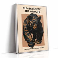 Keep a Respectful Distance, a large black bear with amber and brown fur, head low and shoulders bunched, set on a tan ground under bold black lettering that reads PLEASE RESPECT THE WILDLIFE in a vintage warning sign style, as a framed canvas in a white frame