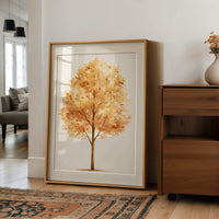 Keeping Its Warmth a Little Longer, a single watercolor tree in amber and rust with a soft brown trunk on a cream ground, the leaves painted in loose soft strokes, in a wood frame on a wall beside a walnut cabinet and an open doorway