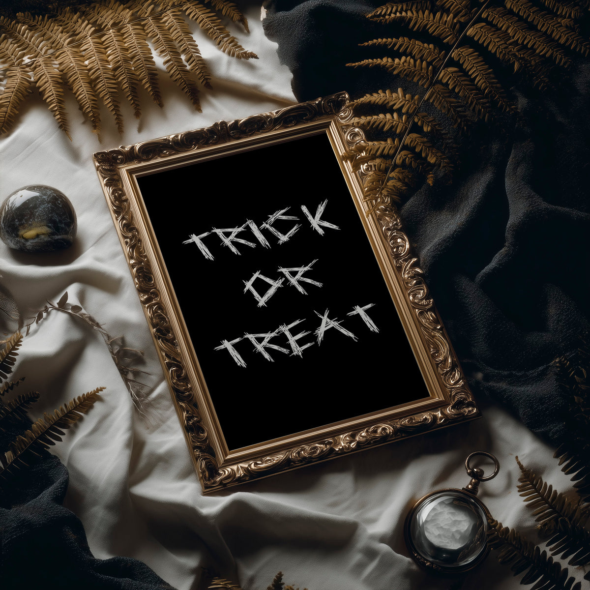 Knock Once for the Sweets, bold chalky white lettering reading TRICK OR TREAT on a solid black ground, hand lettered with a worn brush texture, in an ornate frame on silk cloth beside ferns and a brass compass