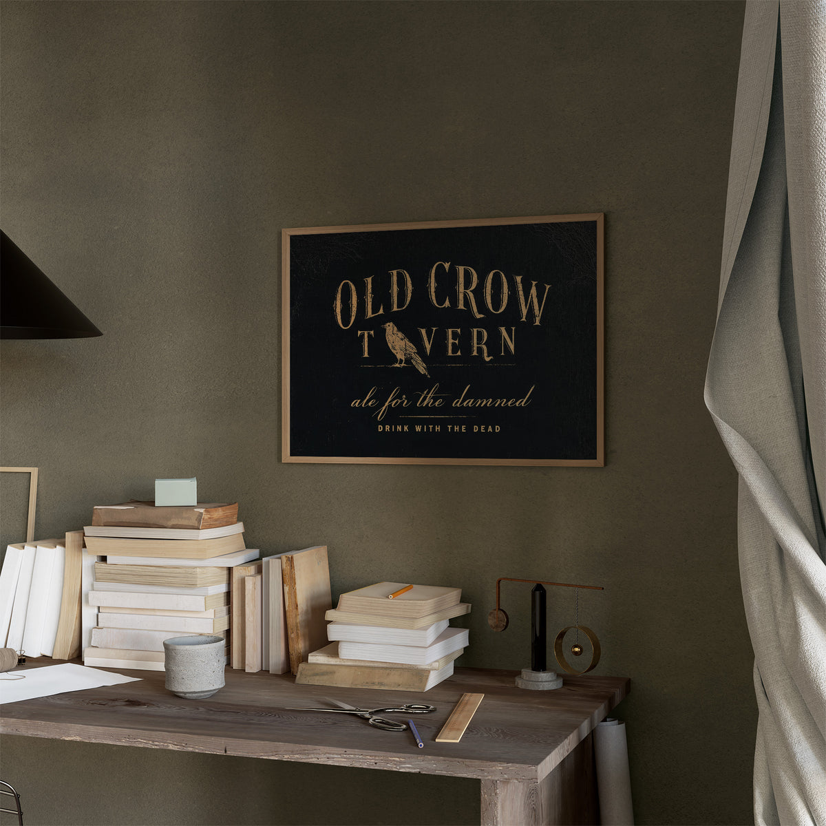 Last Call for the Restless, a black tavern sign lettered in gold with a perched golden bird, painted in black, oxblood and antique gold, in a thin wood frame on a moss green wall above a desk stacked with books