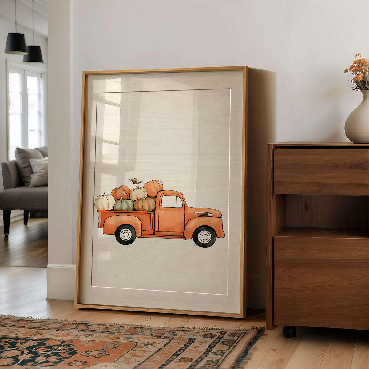 Last Load Up the Orchard Road, a small orange vintage pickup truck loaded with pumpkins and gourds on a cream ground, painted in soft watercolor, in a wood frame on a wall beside a walnut cabinet and an open doorway