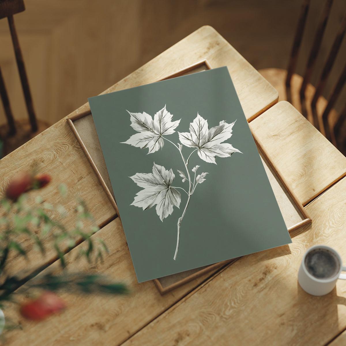 Leaves Kept Pale Against Sage, a sprig of pale maple leaves drawn in bone and white lines on a muted sage green ground, a pressed botanical study with soft, careful shading, lying flat on a light wood table beside a coffee cup and red berries