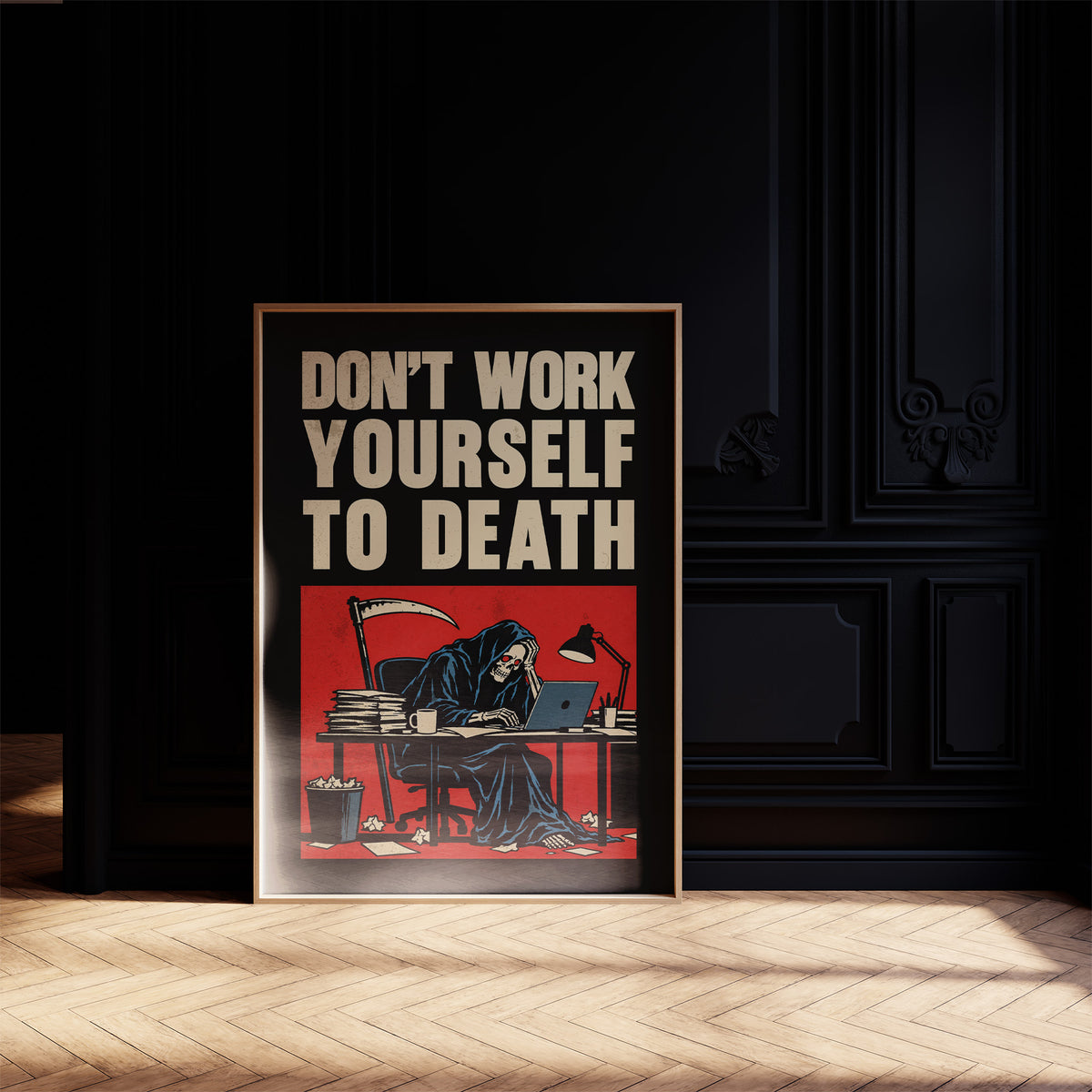Let the Inbox Wait Till Monday, a hooded reaper hunched over a cluttered desk with a laptop and a stack of files, in a red panel with the lettering DON'T WORK YOURSELF TO DEATH in heavy cream capitals on black, in a dark frame on a black paneled wall above a sunlit herringbone floor