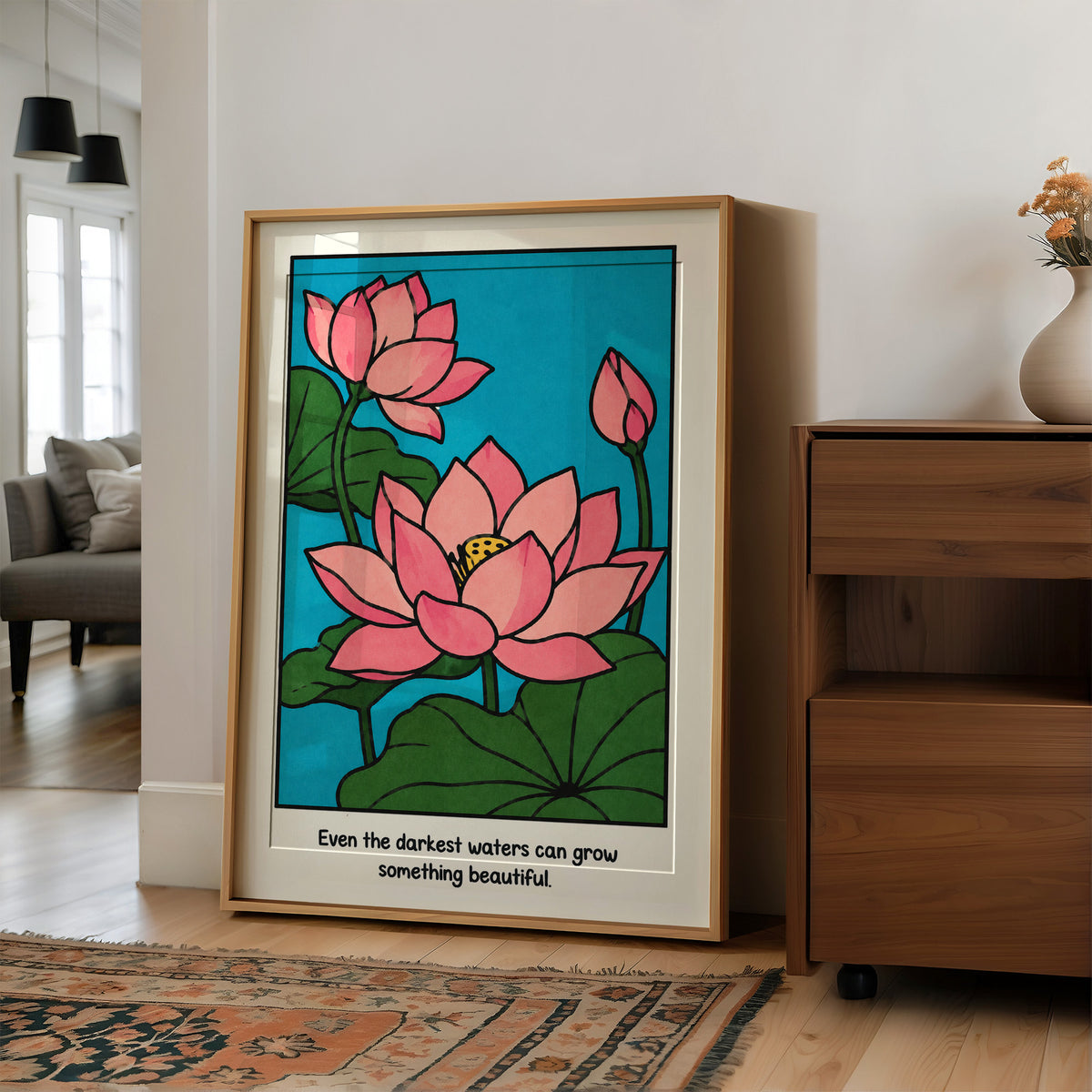 Lotus Rising From Dark Water, a pink lotus flower with a bud and large green leaves on a bright teal pond, with the quote Even the darkest waters can grow something beautiful in small black lettering along the bottom, in a wood frame on a wall beside a walnut cabinet and an open doorway