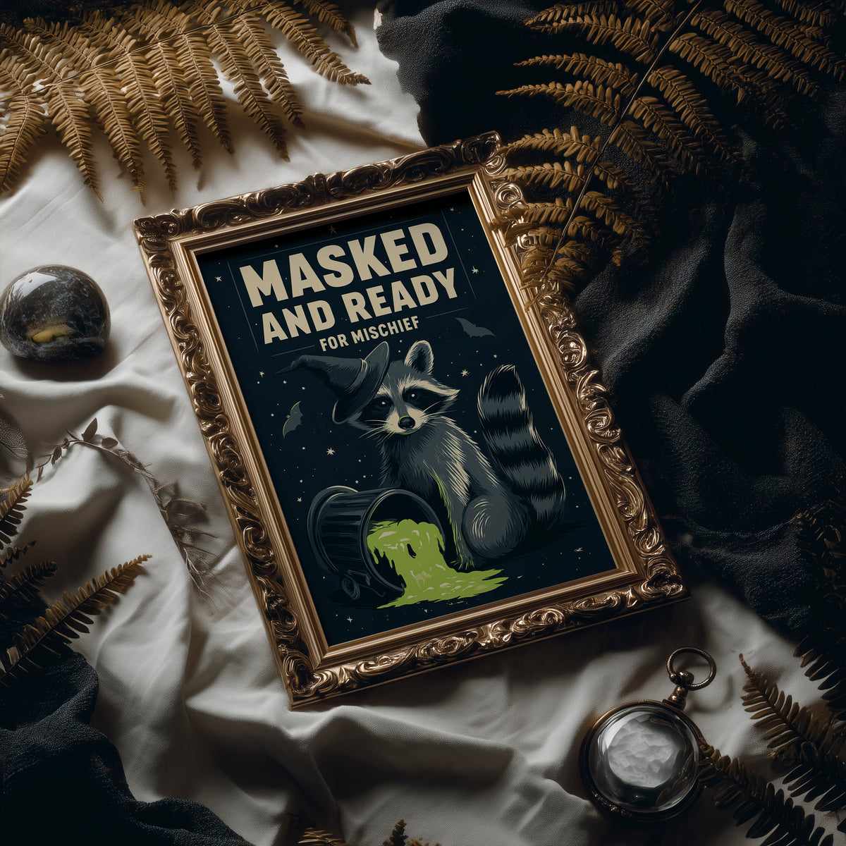 Mischief Wears a Mask, a masked raccoon beside a puddle of glowing green slime under bold cream lettering that reads masked and ready for mischief, in an antique gold frame laid on white linen with ferns and a pocket watch