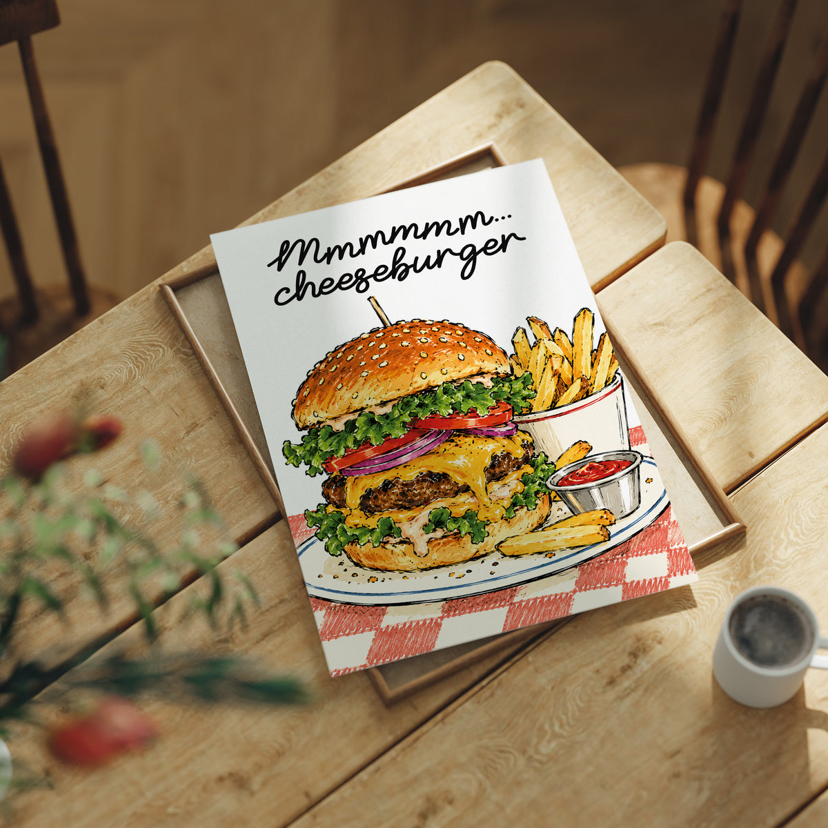 Mmmm Cheeseburger Makes Everything Better, a stacked cheeseburger with lettuce, tomato, cheese and a sesame bun beside fries and ketchup cups on a red and white checkered plate, with the lettering Mmmmm cheeseburger in black script across the top, lying flat on a light wood table beside a coffee cup and red berries