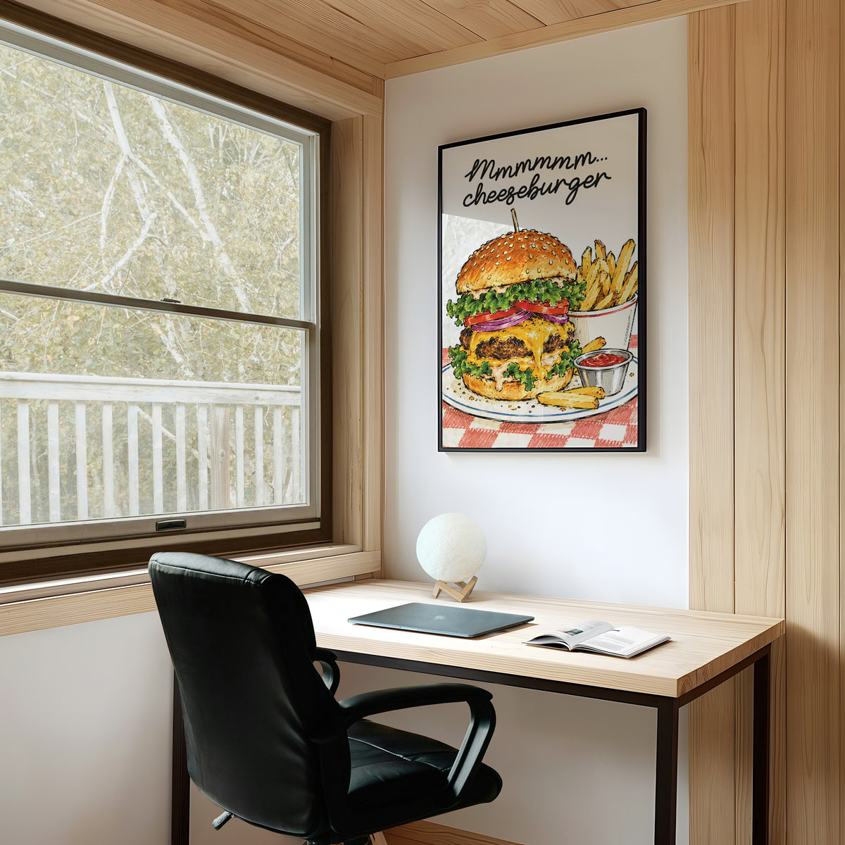 Mmmm Cheeseburger Makes Everything Better, a stacked cheeseburger with lettuce, tomato, cheese and a sesame bun beside fries and ketchup cups on a red and white checkered plate, with the lettering Mmmmm cheeseburger in black script across the top, on a study wall above a writing desk and a black desk chair