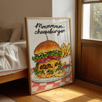 Mmmm Cheeseburger Makes Everything Better, a stacked cheeseburger with lettuce, tomato, cheese and a sesame bun beside fries and ketchup cups on a red and white checkered plate, with the lettering Mmmmm cheeseburger in black script across the top, leaning on a wood floor in a bedroom beside white linen bedding