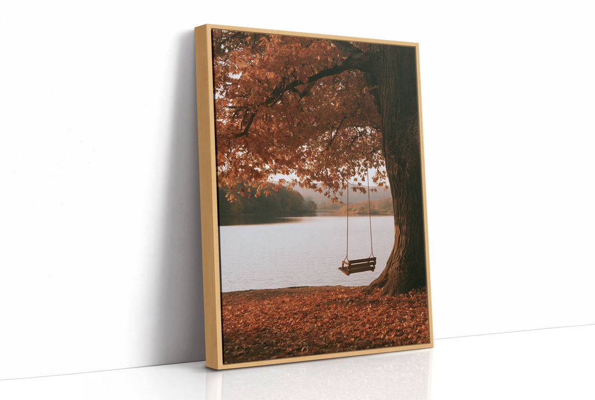 Nobody Has Swung Since Morning, a lone wooden swing hanging from a great tree with orange leaves above a still lake, painted in burnt orange, rust and misty gray, as a framed canvas in a natural wood frame