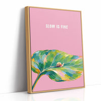 Nothing Here Is Rushed, a green leaf curling across the lower half of a blush pink ground with a small snail resting on its curve, with a pale line of lettering above, in a loose watercolor style painted in blush pink, green and soft gold, as a framed canvas in a natural wood frame