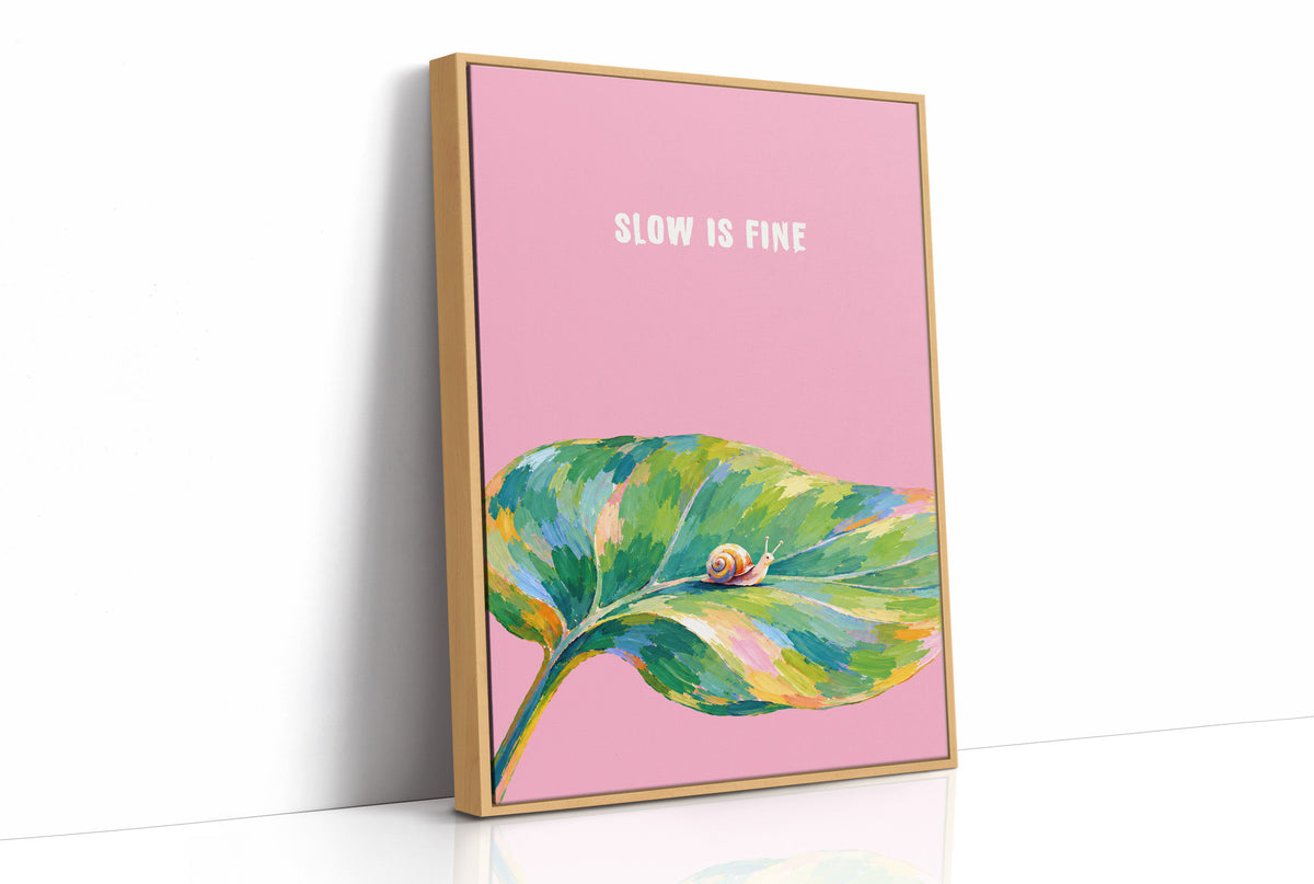 Nothing Here Is Rushed, a green leaf curling across the lower half of a blush pink ground with a small snail resting on its curve, with a pale line of lettering above, in a loose watercolor style painted in blush pink, green and soft gold, as a framed canvas in a natural wood frame
