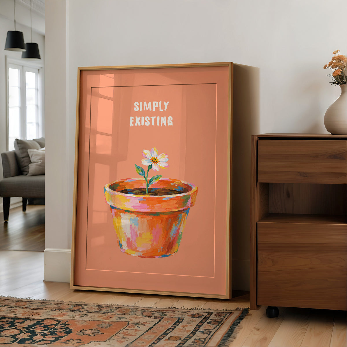 One Small Bloom in Clay, a single white flower rising from a painted clay pot in coral, gold and pink brushstrokes, on a peach ground with two lines of bold pale lettering above, in a loose painterly style, in a wood frame on a wall beside a walnut cabinet and an open doorway