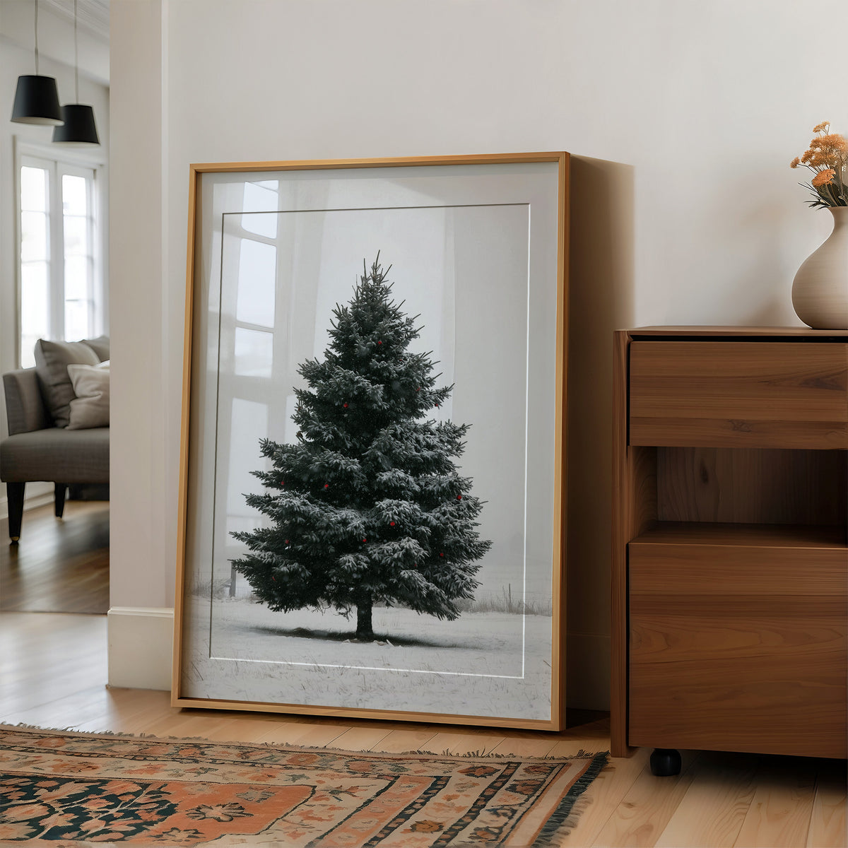 One Spruce Holds the Snowfield, a single dark spruce standing alone in a snowy field under a pale gray sky, painted in forest green, snow white and soft gray, in a wood frame on a wall beside a walnut cabinet and an open doorway
