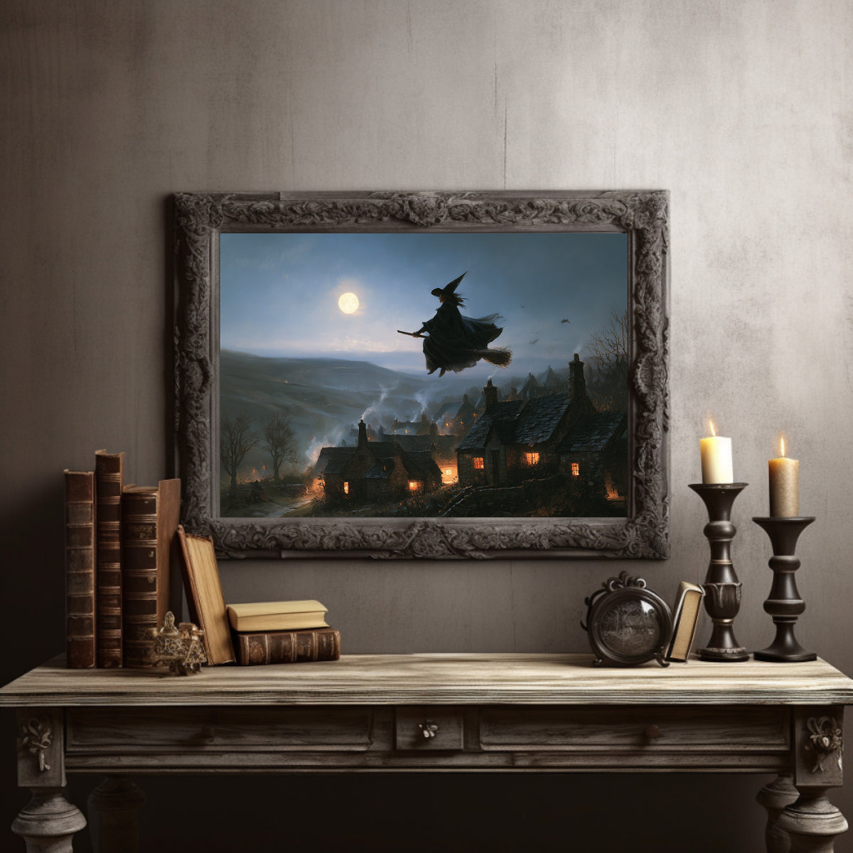 Over the Lantern Village, a witch flying across a full moon above a lantern lit village on a misty hillside, painted in midnight blue, pale moon gold and soft smoke gray, in a dark carved frame on a gray wall above a console table with candlesticks and old books