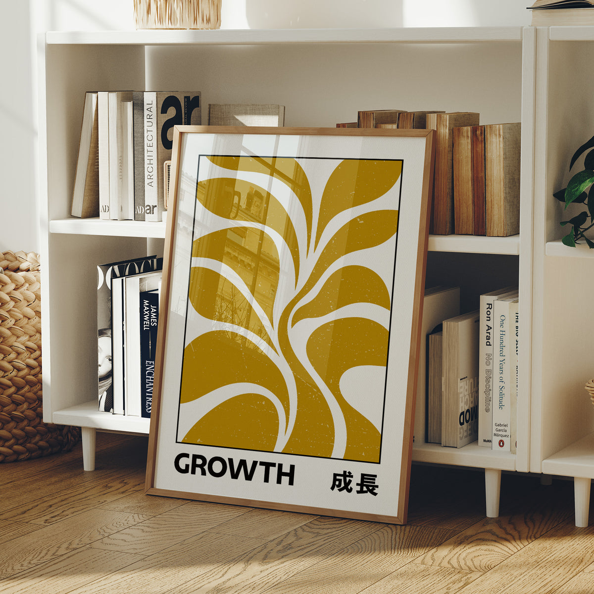 Patient Leaves Turning Toward Light, a stylized mustard leaf motif in curved shapes on a cream ground, with the word GROWTH in black capitals and a small Japanese word beside it, in a wood frame on a white bookshelf beside stacked books and a small basket