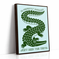 Perfectly Harmless, Mind the Teeth, a deep green crocodile curling down a pale mint ground, with a bold hand lettered line above reading I'M PERFECTLY HARMLESS and one below reading JUST MIND THE TEETH, as a framed canvas in a brown frame