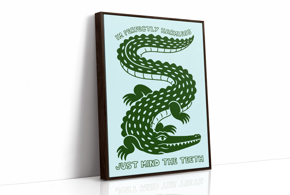 Perfectly Harmless, Mind the Teeth, a deep green crocodile curling down a pale mint ground, with a bold hand lettered line above reading I'M PERFECTLY HARMLESS and one below reading JUST MIND THE TEETH, as a framed canvas in a brown frame